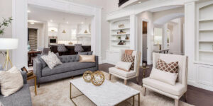 Modern living room with neutral tones, elegant furniture, built-in shelving, and an open view into a bright kitchen.