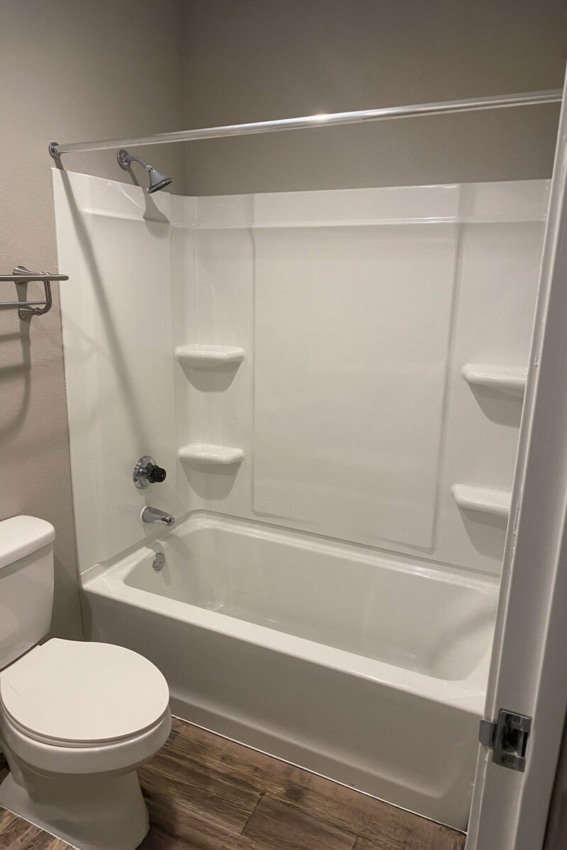 A newly installed white bathtub and shower surround with clean fixtures and a toilet beside it.