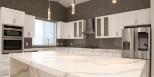 Modern kitchen with white cabinets, large marble-patterned island, and stainless steel appliances.