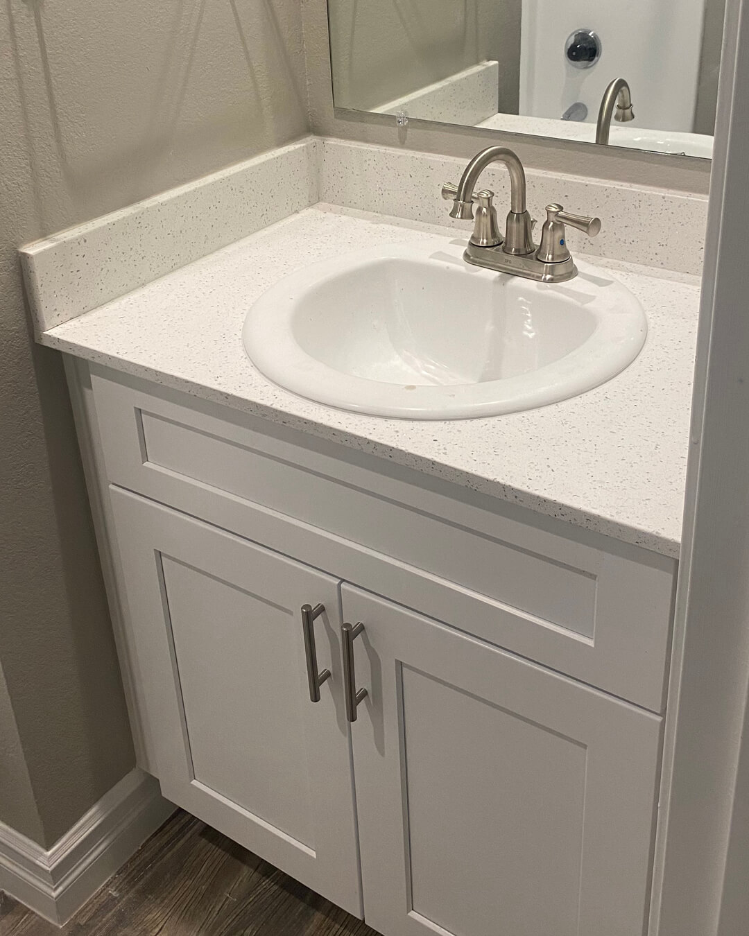 White bathroom vanity with speckled quartz countertop and chrome faucet.
