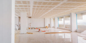An unfinished commercial interior under renovation, with drywall installation and construction materials scattered on the floor.
