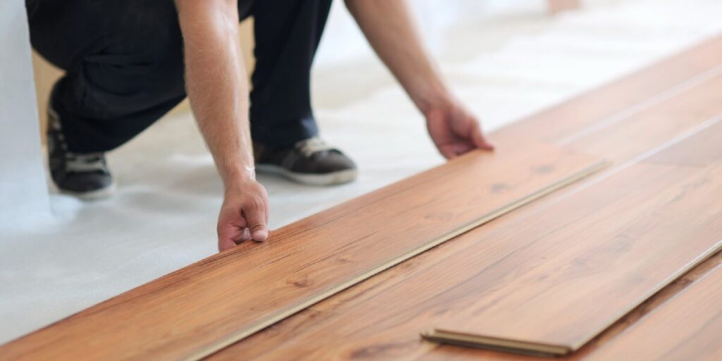 A person installing wood flooring planks in a home, representing flooring selection, home renovation, durability, interior upgrades, and practical living solutions.