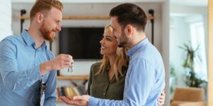 A smiling man hands a set of keys to a happy couple standing together in a bright modern apartment.