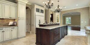 Elegant kitchen with cream cabinetry, a dark wood island and two crystal chandeliers overhead.