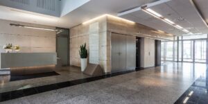 A modern building lobby with polished stone floors, a reception desk, and glass entry doors.